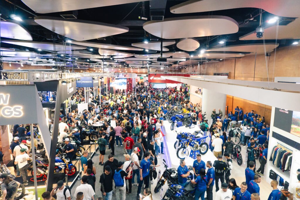 Visitantes recorriendo una feria de motocicletas con exhibiciones de diferentes modelos y espacios culturales.